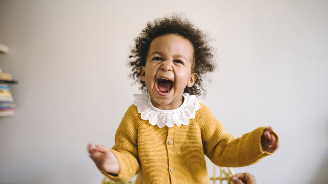 En jätteglad liten tjej i gul tröja och med vit krage i närbild. 