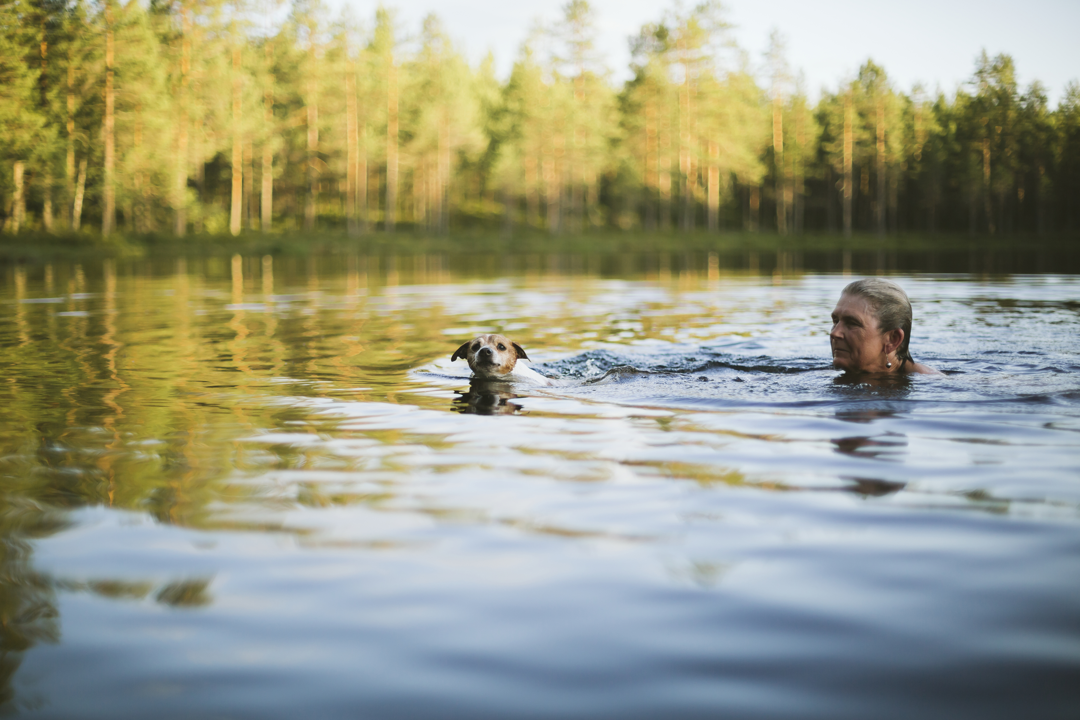 En kvinna och en hund badar i en sjö omgiven av träd 