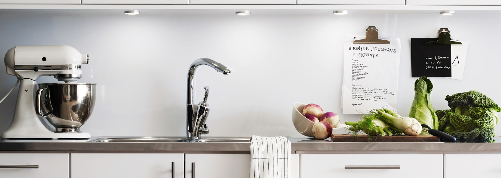 Närbild på ett vitt kök med en bänk med grönsaker på. 