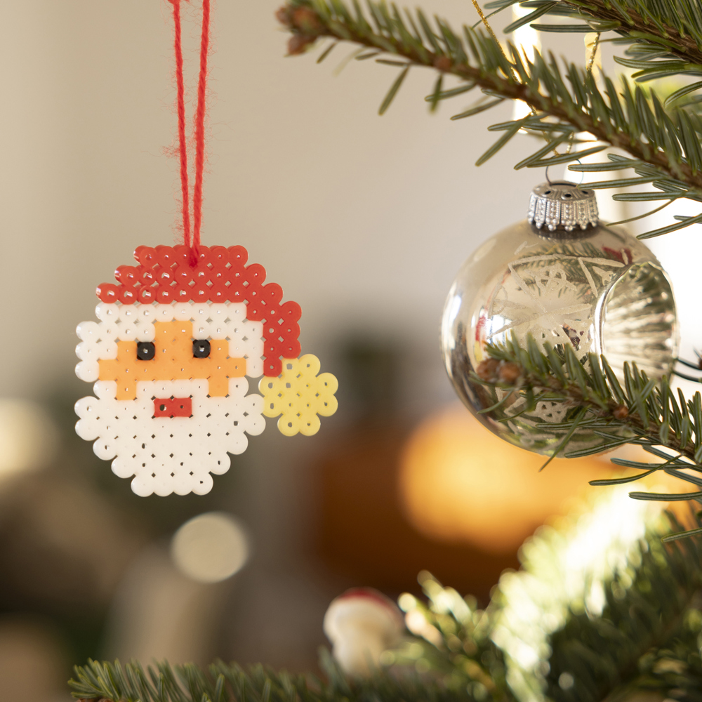 En pärlad jultomte som hänger som dekoration i granen.