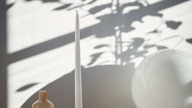 En närbild på en hemmiljö med ett stileben med ljusstake, vit glaslampa och några inredningsdetaljer. 