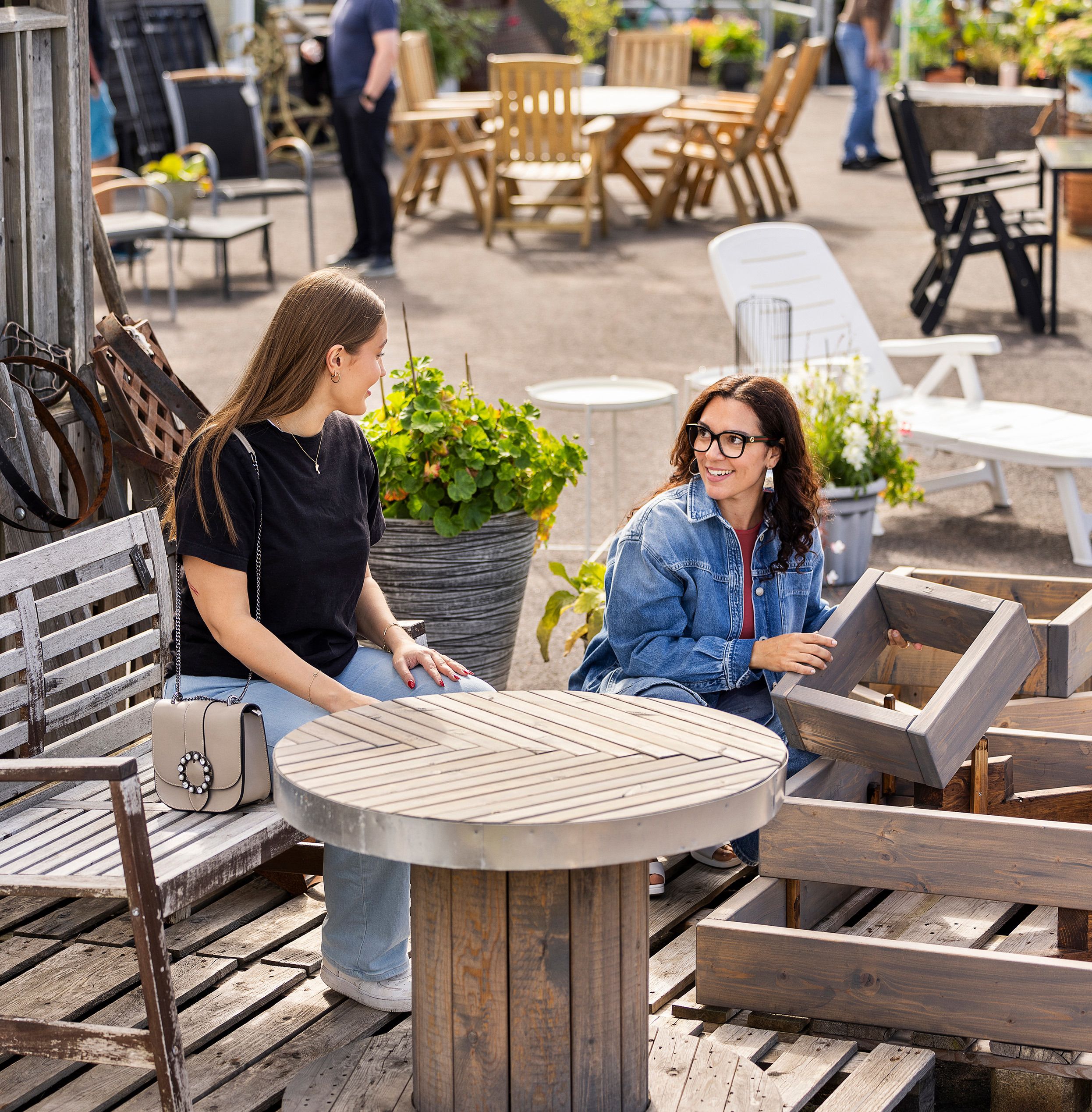 Två kvinnor samtalar vid ett träbord vid ett återbruk