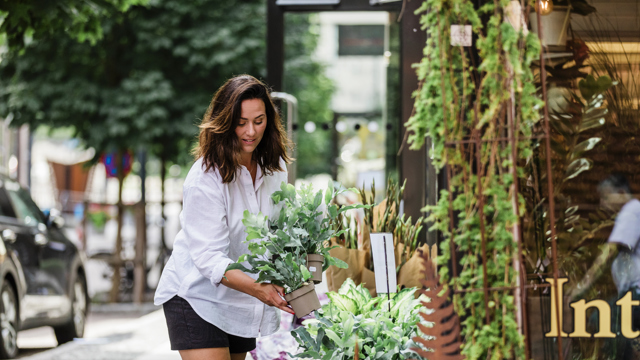 En kvinna kikar på blommor en solig sommardag utanför en Interflora butik. 