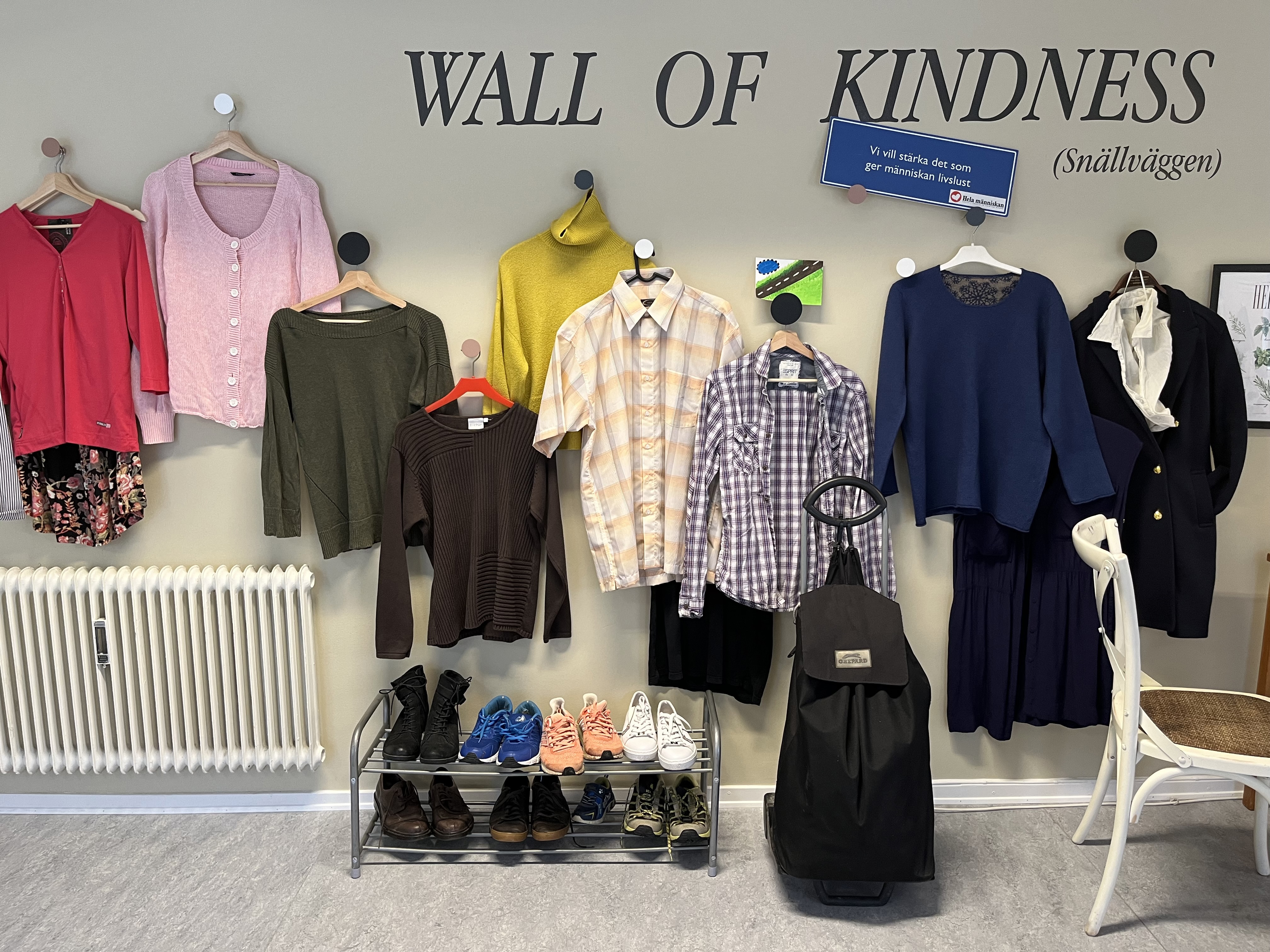 En vägg där det hänger kläder på galgar och står en text med orden Wall of Kindness.