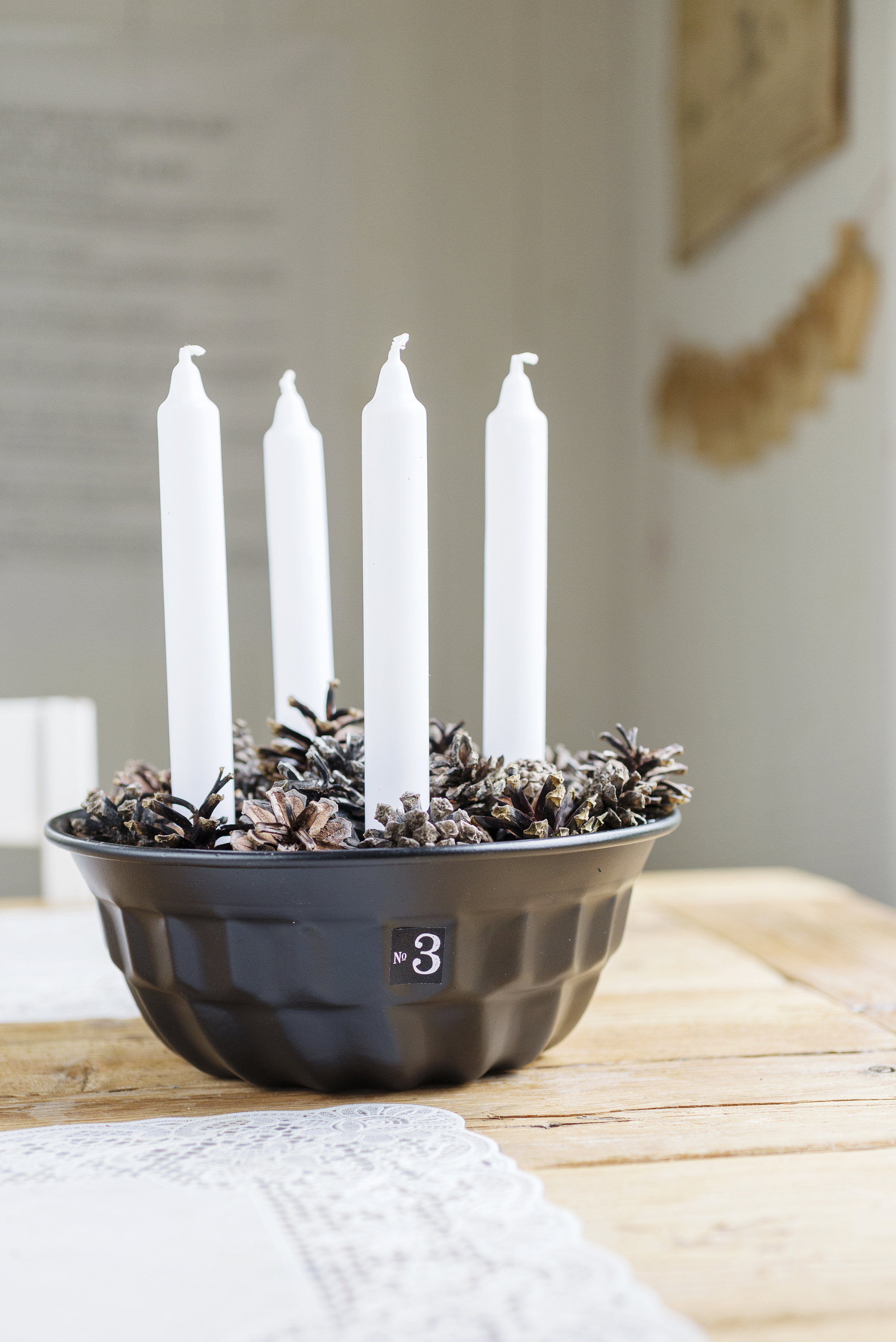 Fyra ljus i en bakform med kottar som dekoration. 