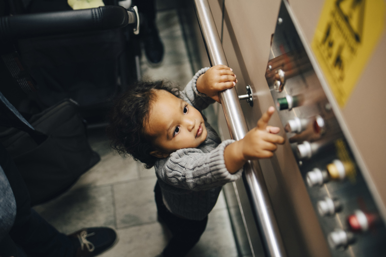 Ett litet barn sträcker sig och är på väg att trycka på en våningsknapp i en hiss.