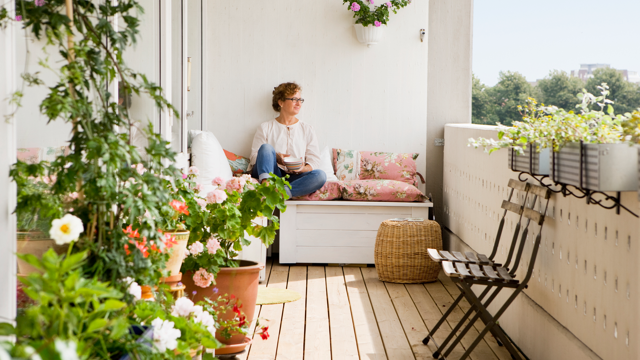 Kvinna njuter på sin balkong omgiven av växter en solig sommar dag. 