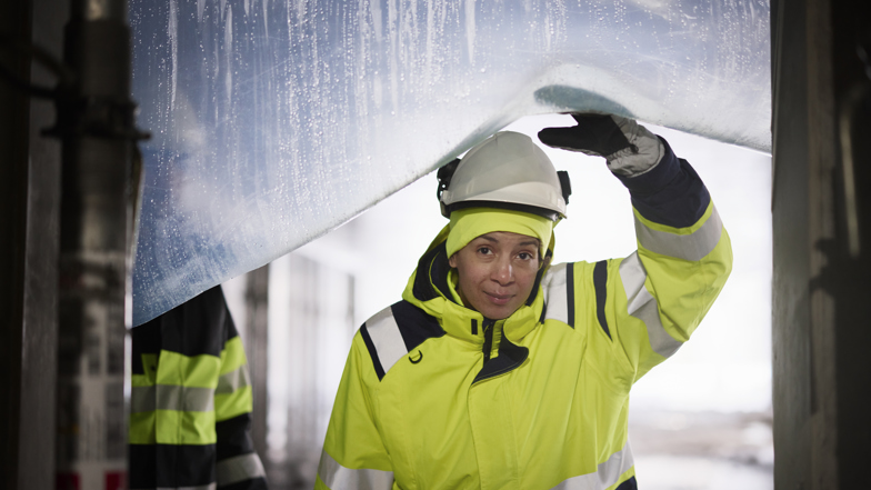 Kvinna med bygghjälm med en byggställning i bakgrunden. 