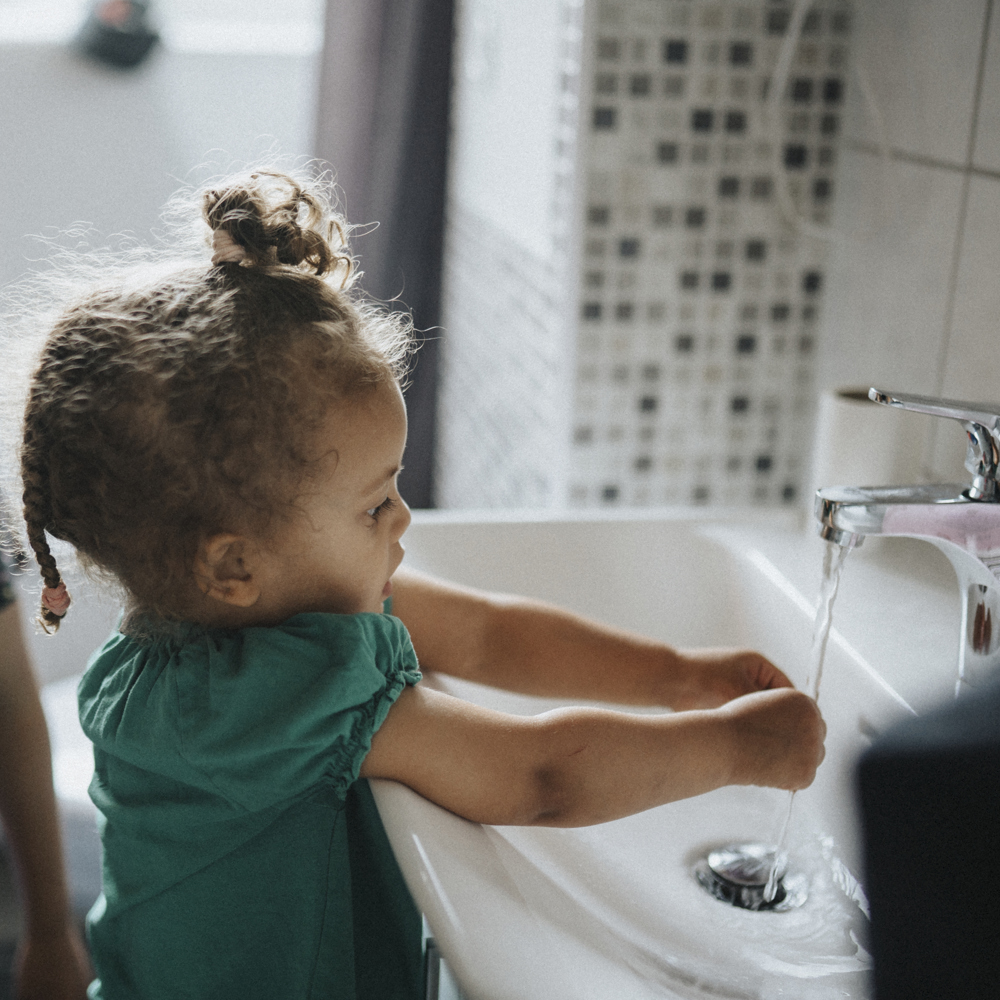 Ett barn tvättar händerna i ett handfat 